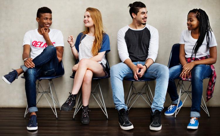 four teens sitting in chairs talking and smiling